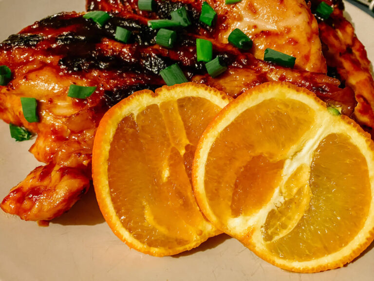 Close up of BBQ orange chicken with orange slices on a white plate