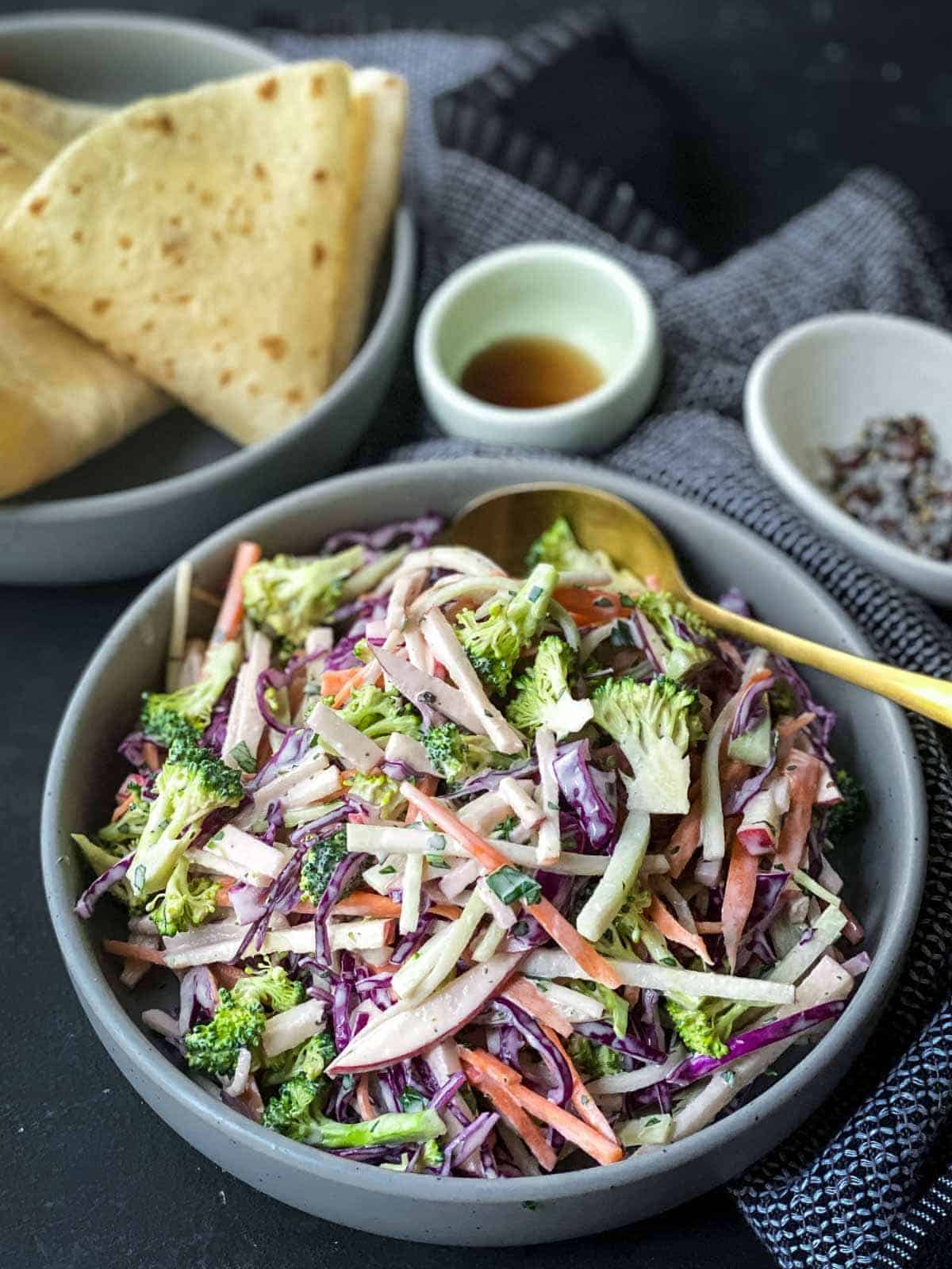 broccoli slaw in large bowl with flatbreads in the background