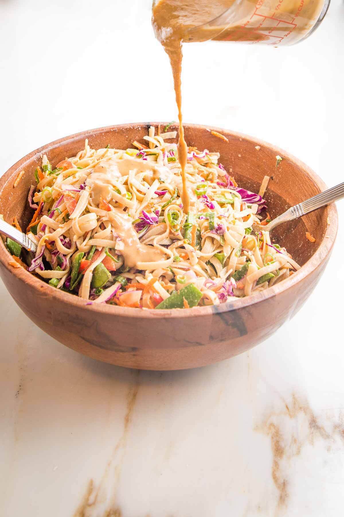 person pouring sauce into a wooden bowl of cold noodles