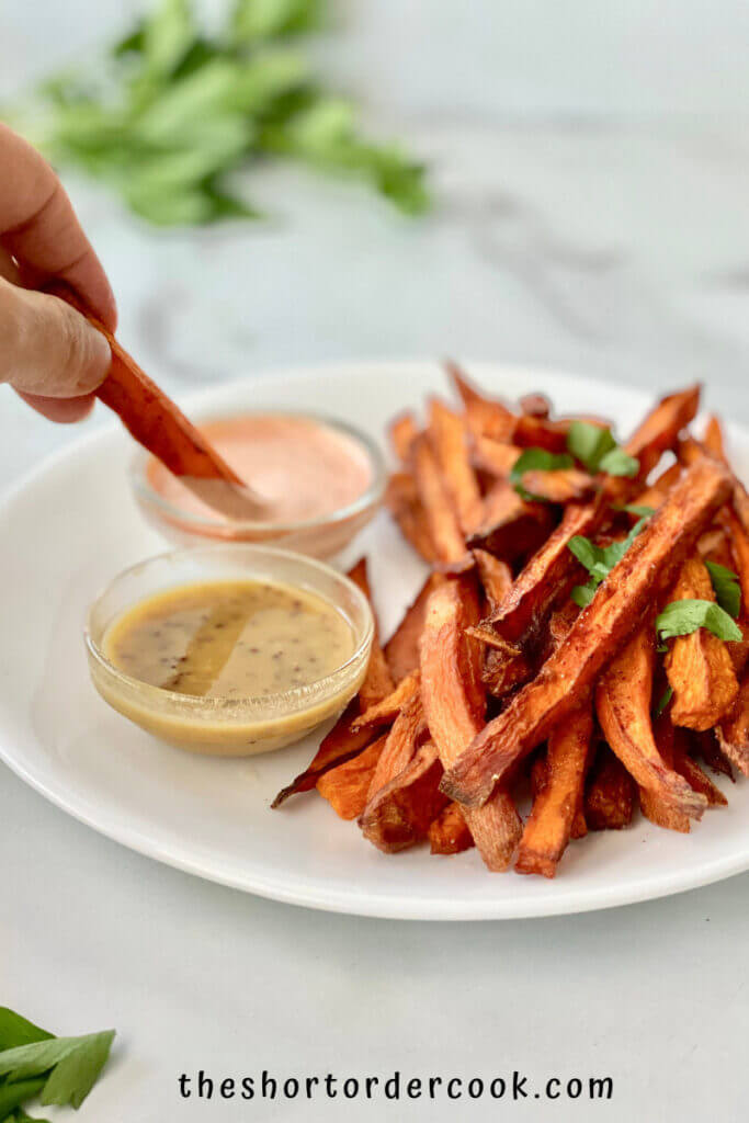 deep fried sweet potato fries ready to eat on a plate with hand dipping on into a dipping sauce