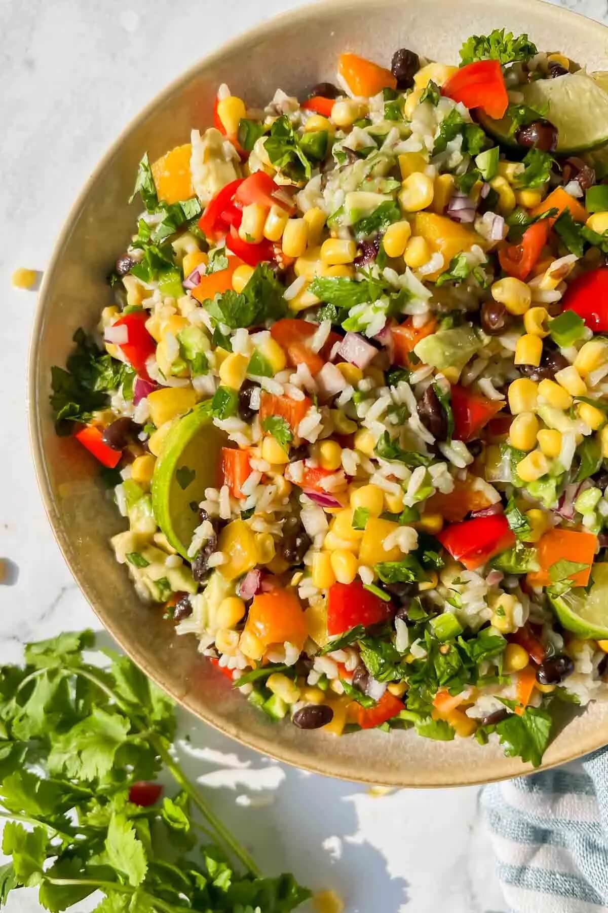 bright coloured rice salad dish in a large bowl with salad leaves on the side