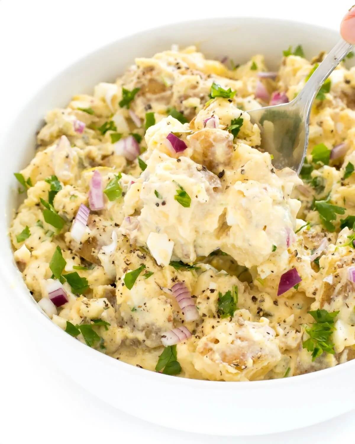 large white bowl of creamy potato salad with spoon