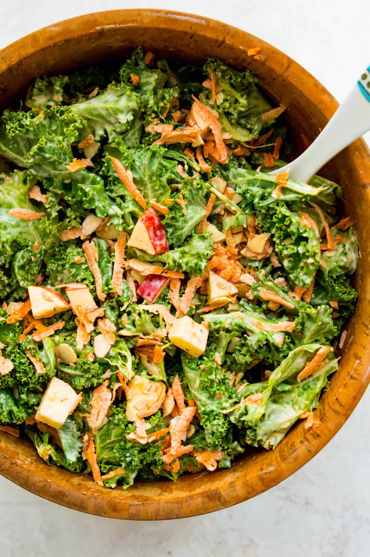 large wooden bowl with spoon filled with kale slaw salad