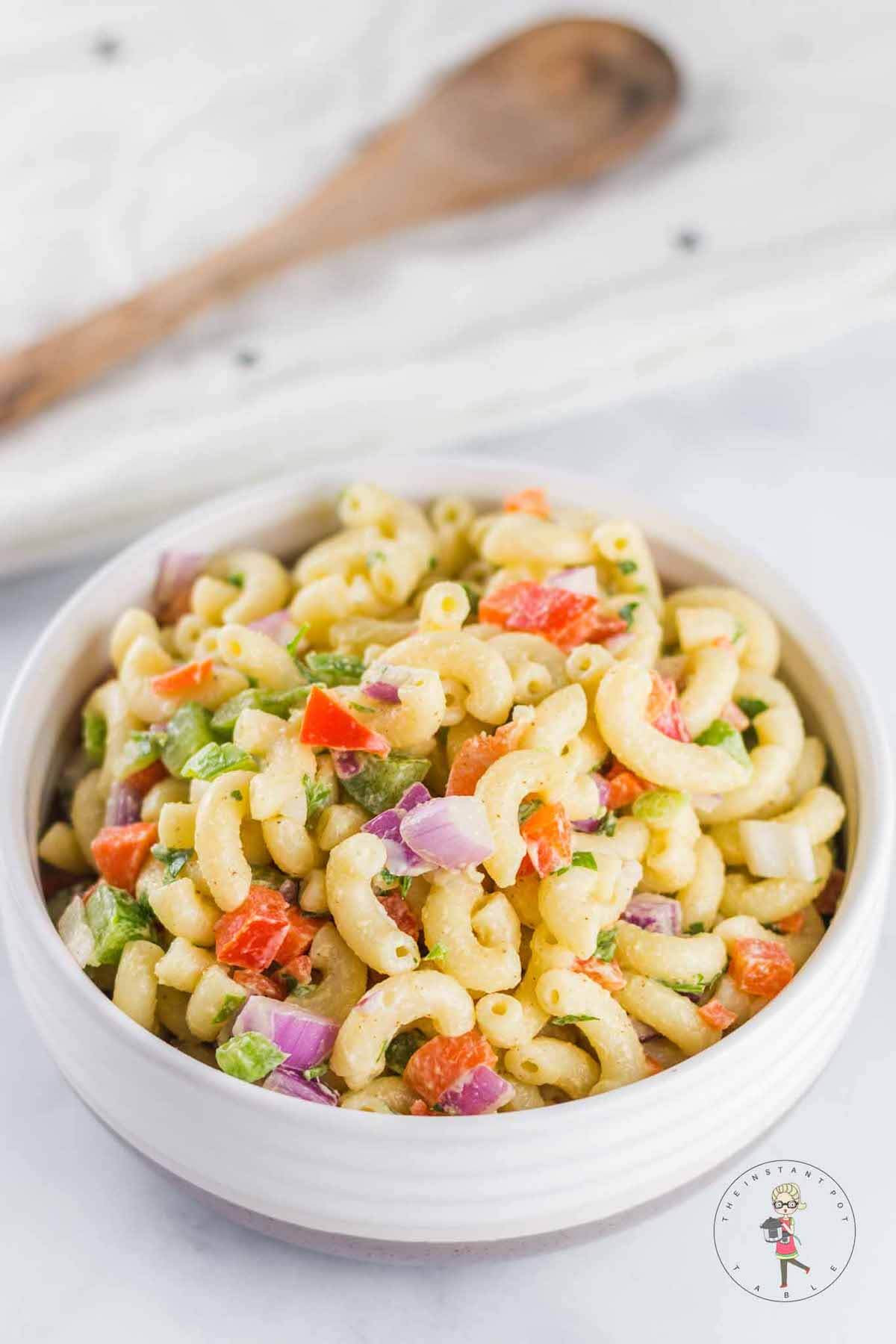 serving of macaroni salad in a white bowl with wooden spoon in background