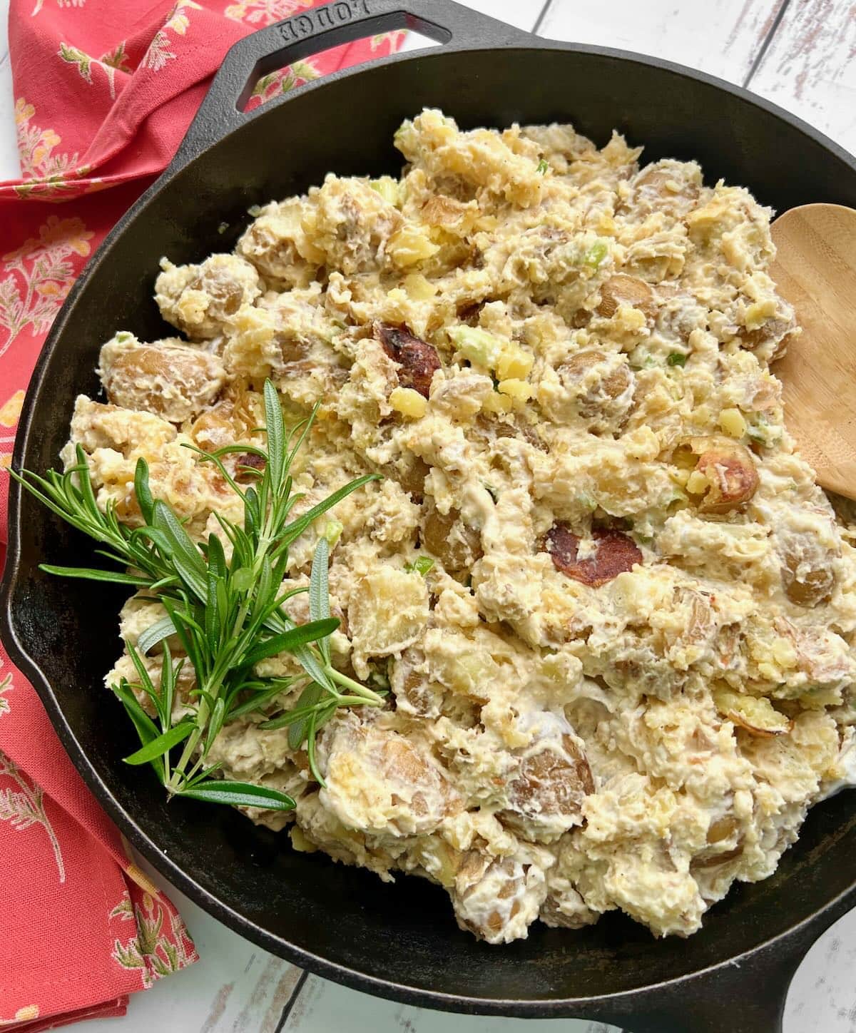 smoked potato salad in a large black skillet with a red cloth to the side