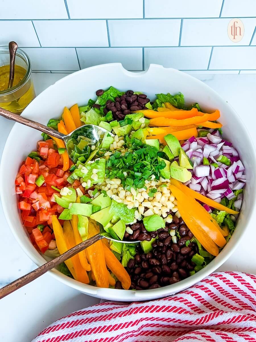 large white bowl with colourful salad and a spoon, sitting next to a red cloth