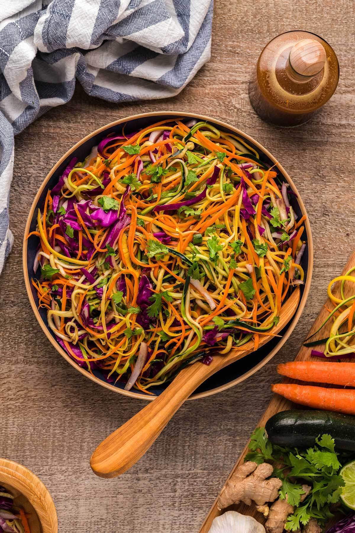 large brown bowl with wooden serving spoon filled with asian zoodle salad