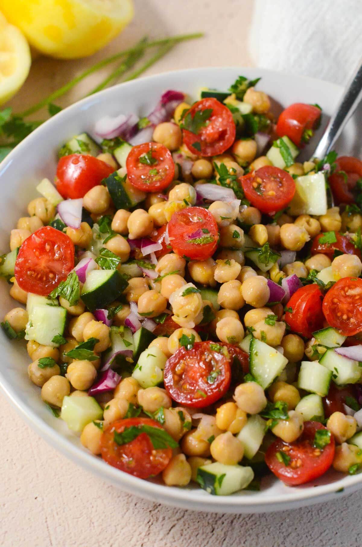 large white bowl filled with chickpea salad and a spoon sticking out