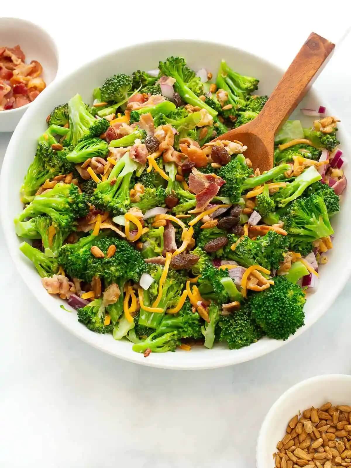 large white bowl with wooden spoon filled with broccoli salad