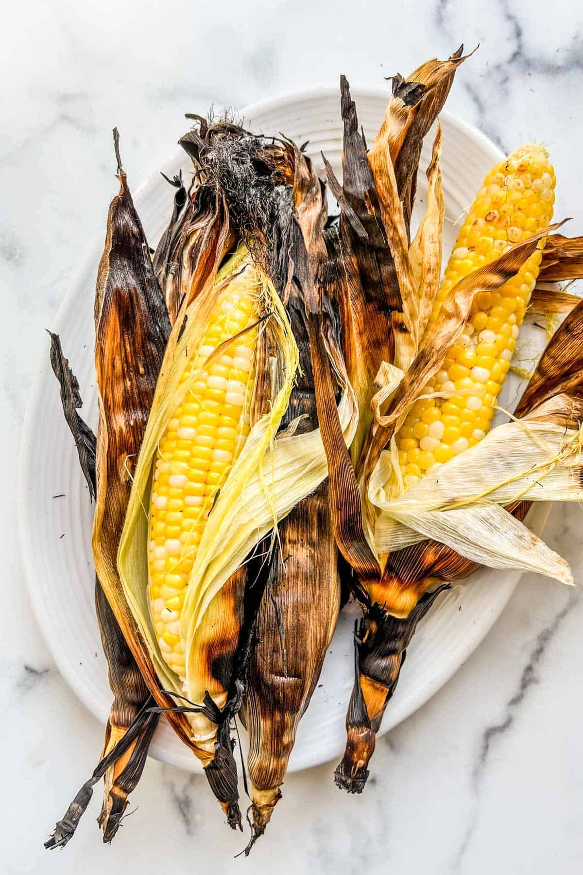 a pile of corn cobs in husks on a plate after grilling