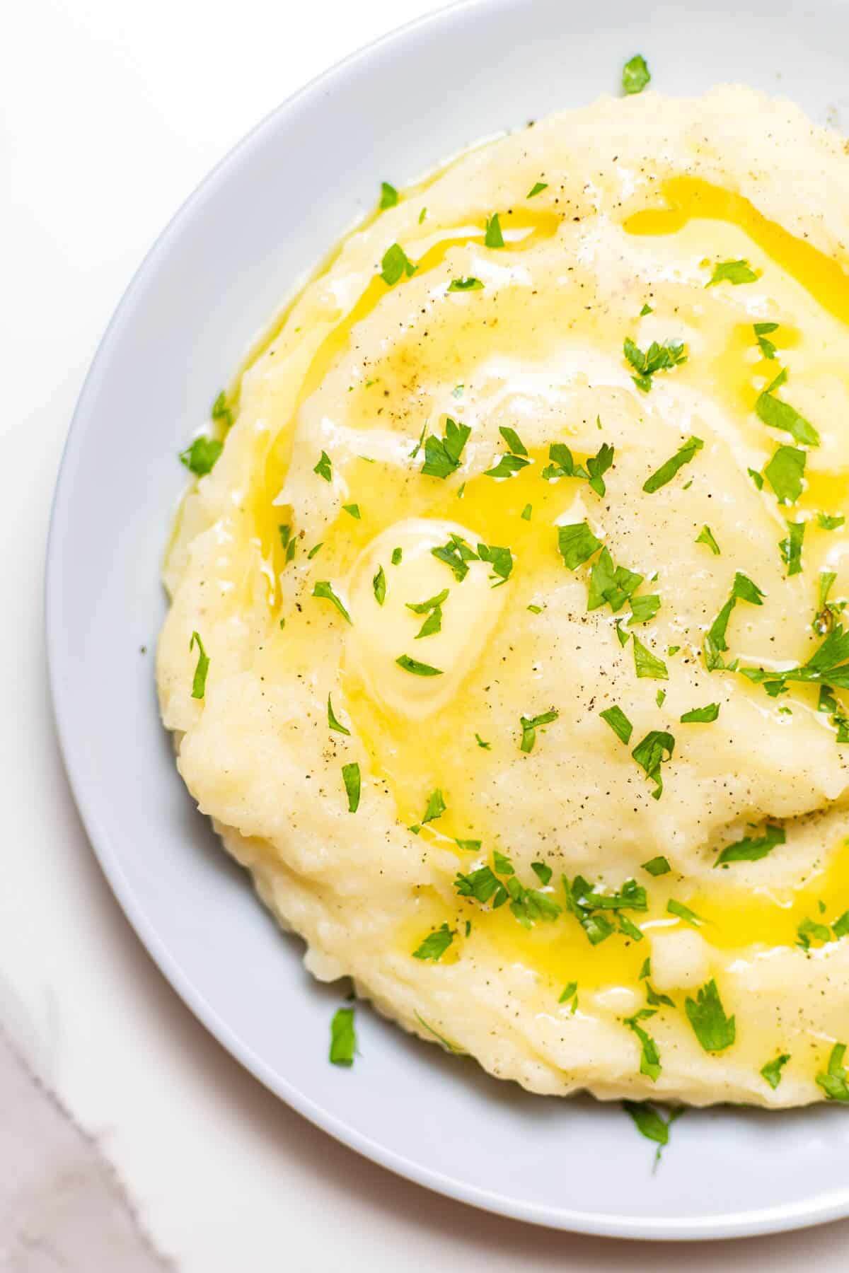 white plate with creamy garlic mashed potato sprinkled with herbs