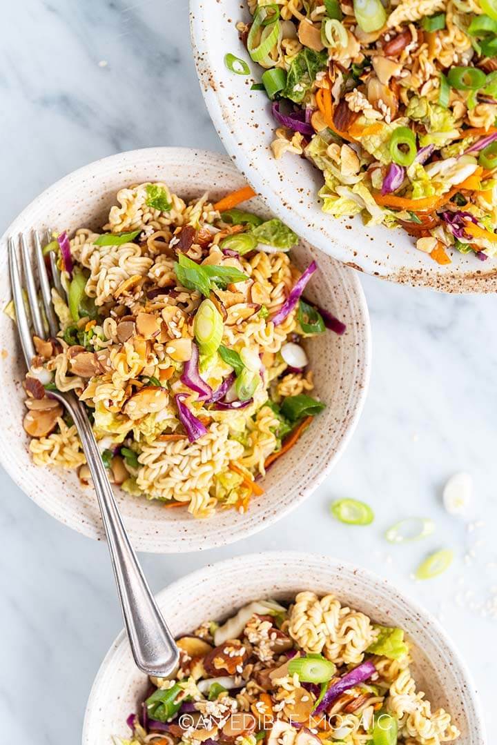 three white bowls on a marble table with ramen noodle salad