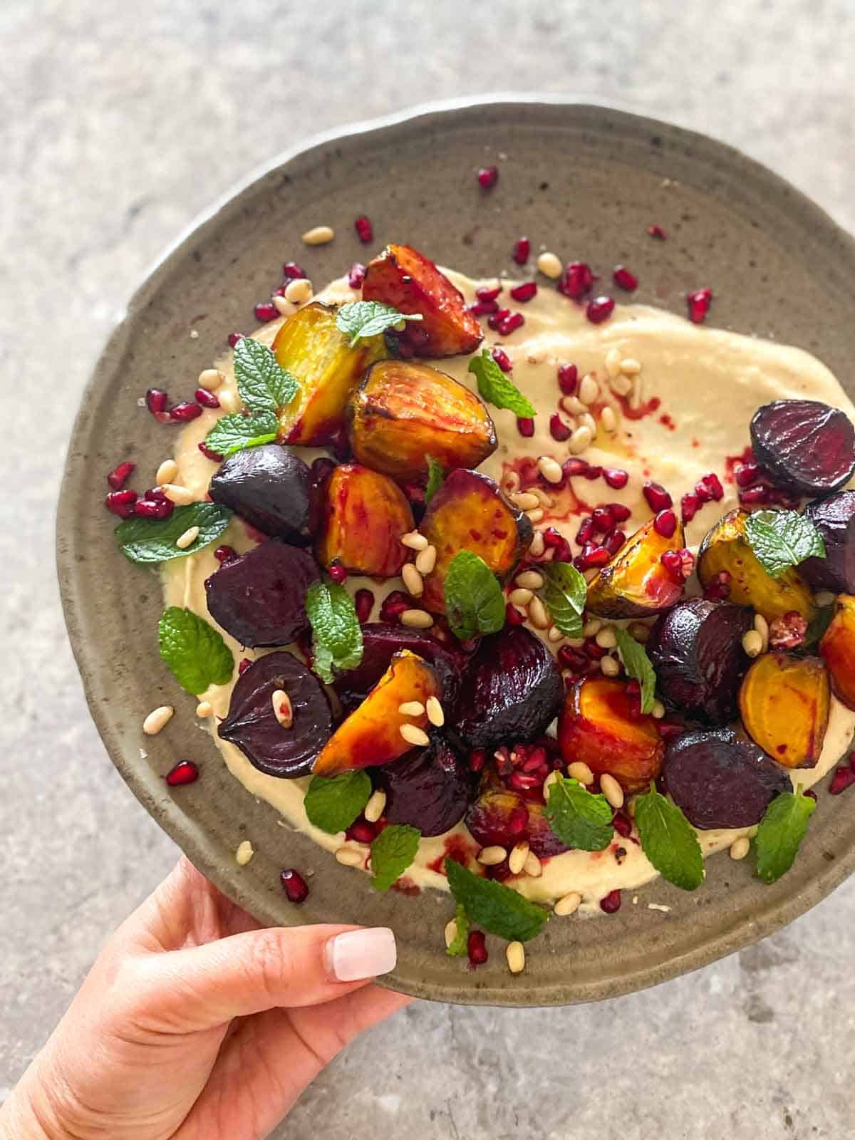 woman holding a large plate with hummus and roasted baby beets