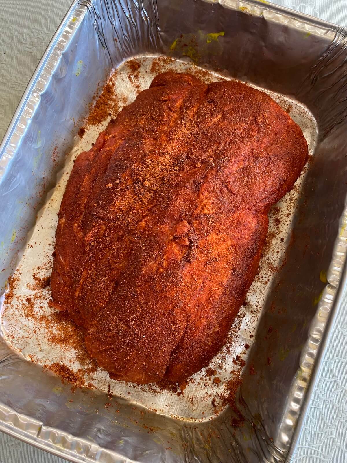 pork collar butt in foil tray with meat rub ready for smoking.