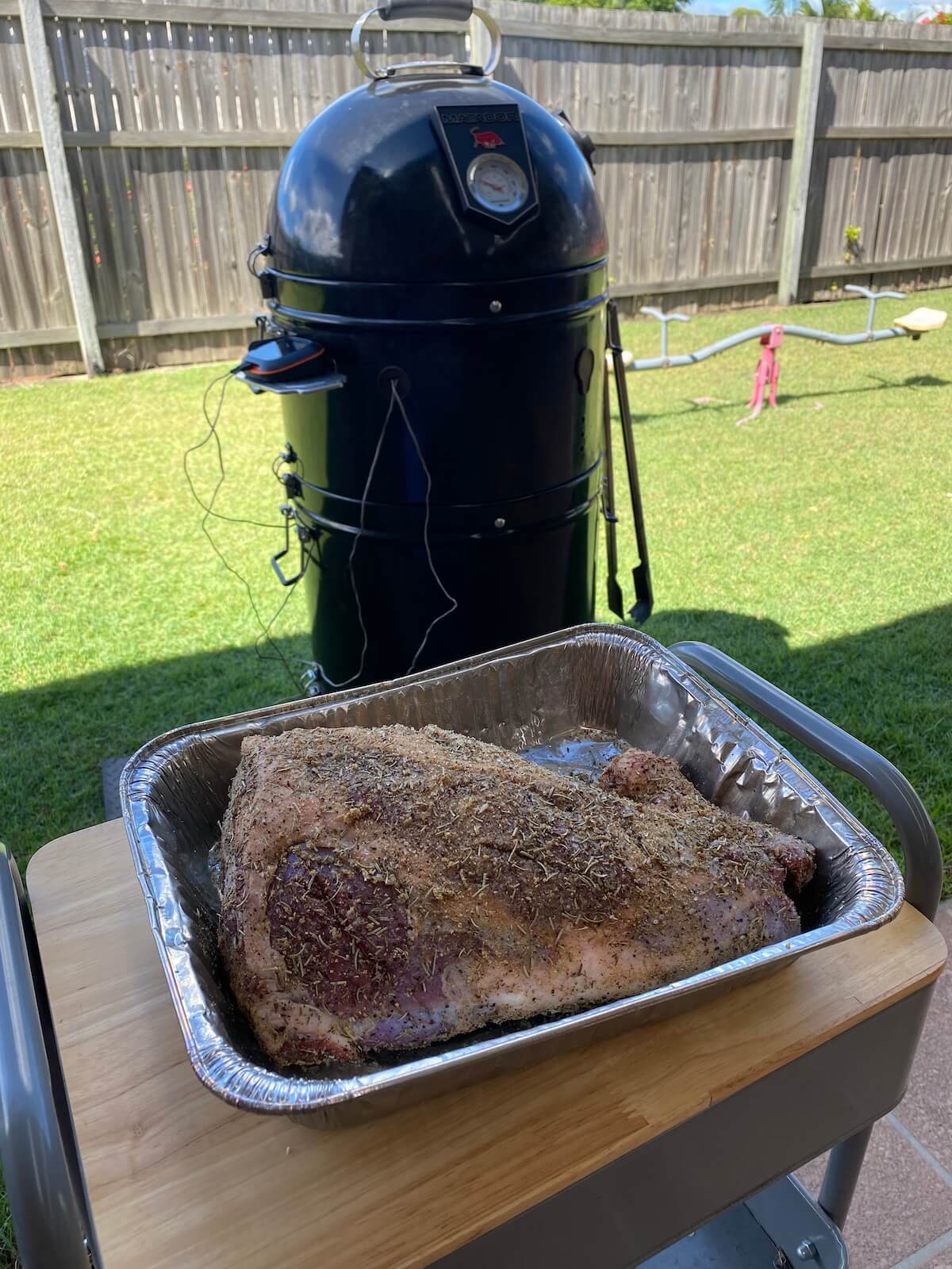 tray with prepared meat and a bullet smoker in the background