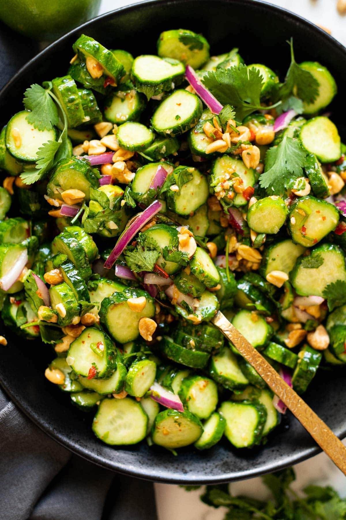 thai cucumber salad in a black bowl and wooden serving spoon