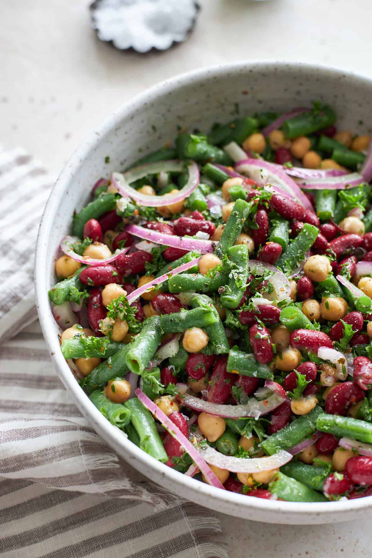 large white bowl of three bean salad with a pinstripe cloth