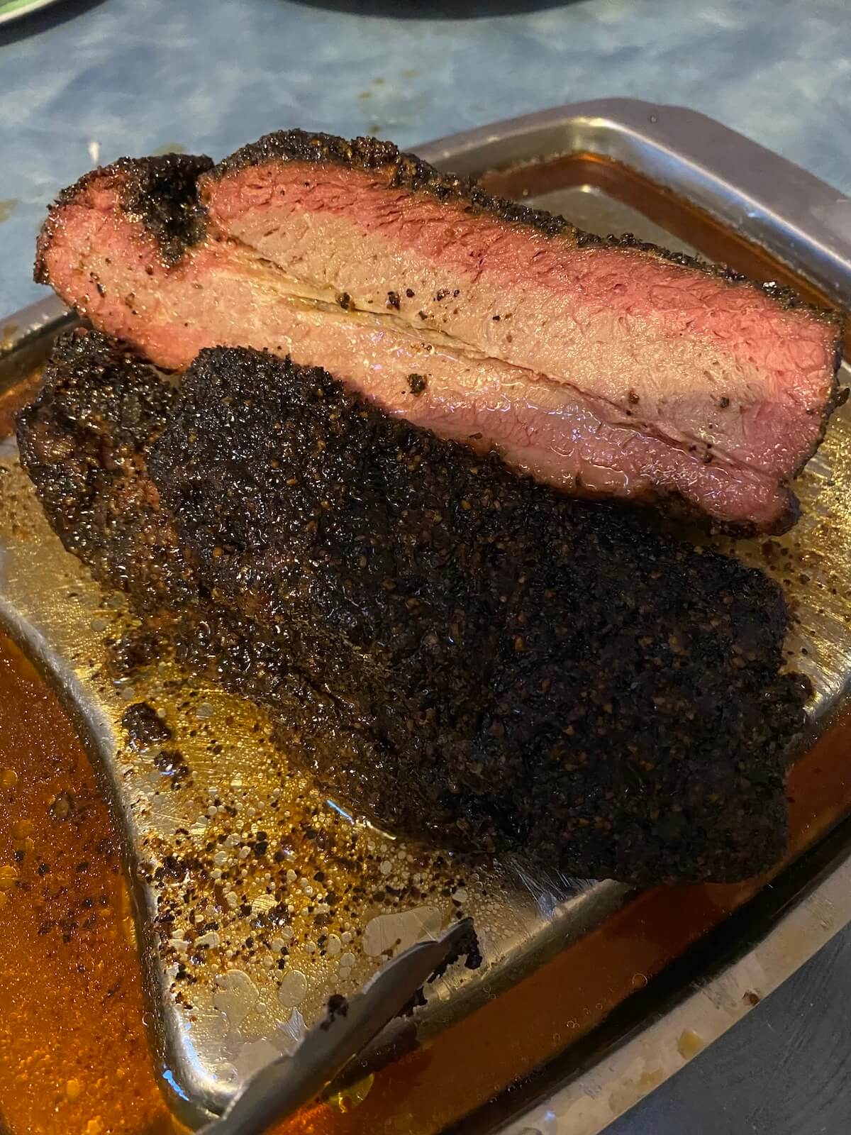 Smoke ring around edges of smoked brisket, carved into slices on silver tray.