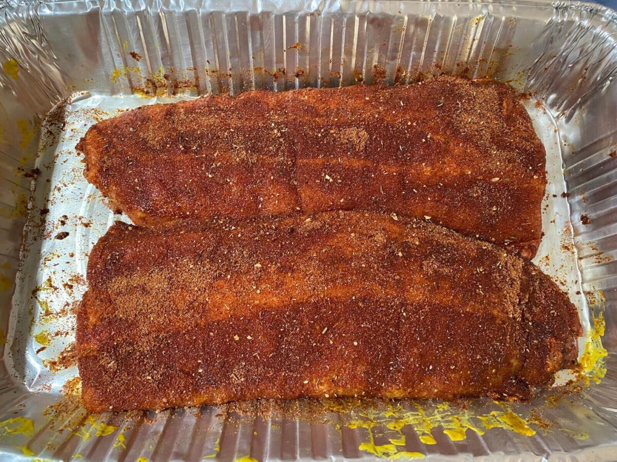 two pork ribs in a foil tray with dry rub