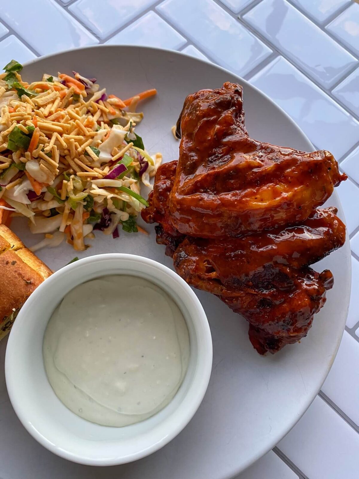 buffalo chicken wings on white plate with salad and small bowl of blue cheese sauce.