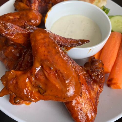 smoked buffalo wings with blue cheese sauce and carrot sticks on a plate.