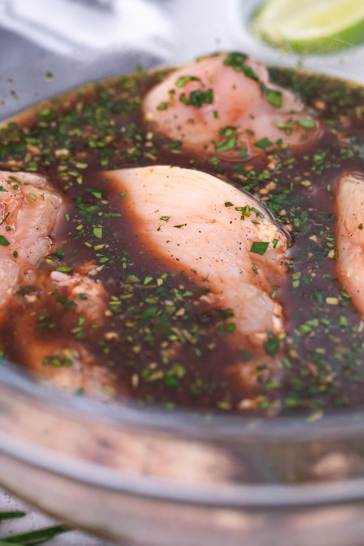 chicken breasts soaking in a glass bowl in a marinade.