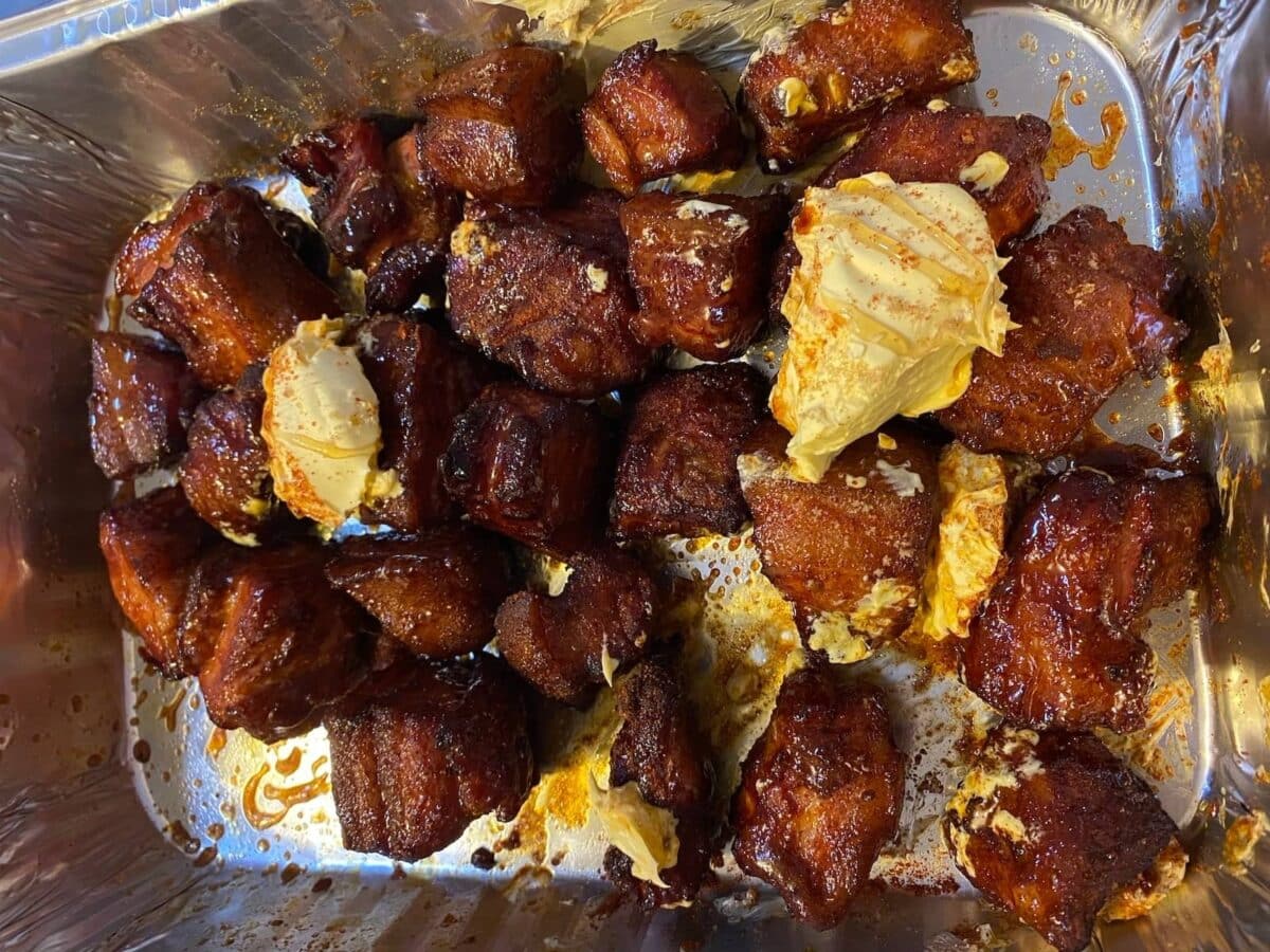 pork belly burnt ends in foil tray with bbq sauce and butter heaped on top.
