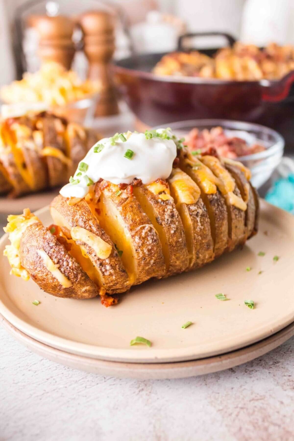 close up on a hasselback potato on a tan coloured plate, with sour cream on top.