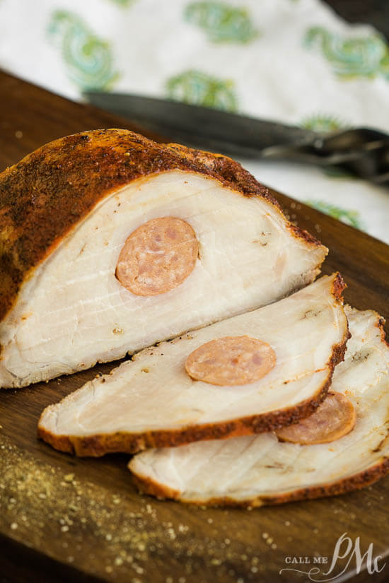 stuffed pork loin on wooden chopping board with 2 pieces sliced.