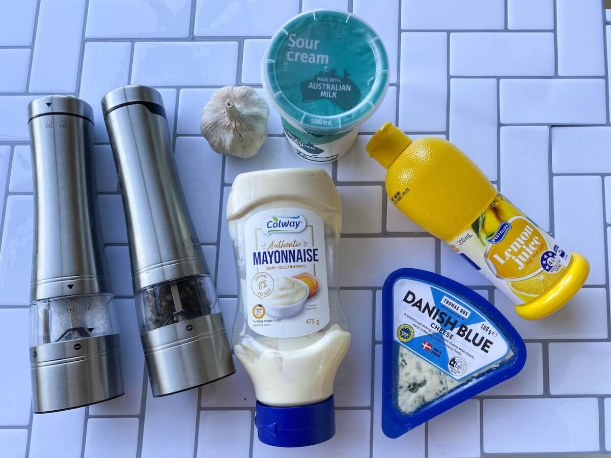 ingredients for blue cheese sauce on a white tiled background including blue cheese, mayonnaise, salt and pepper, sour cream and lemon juice.