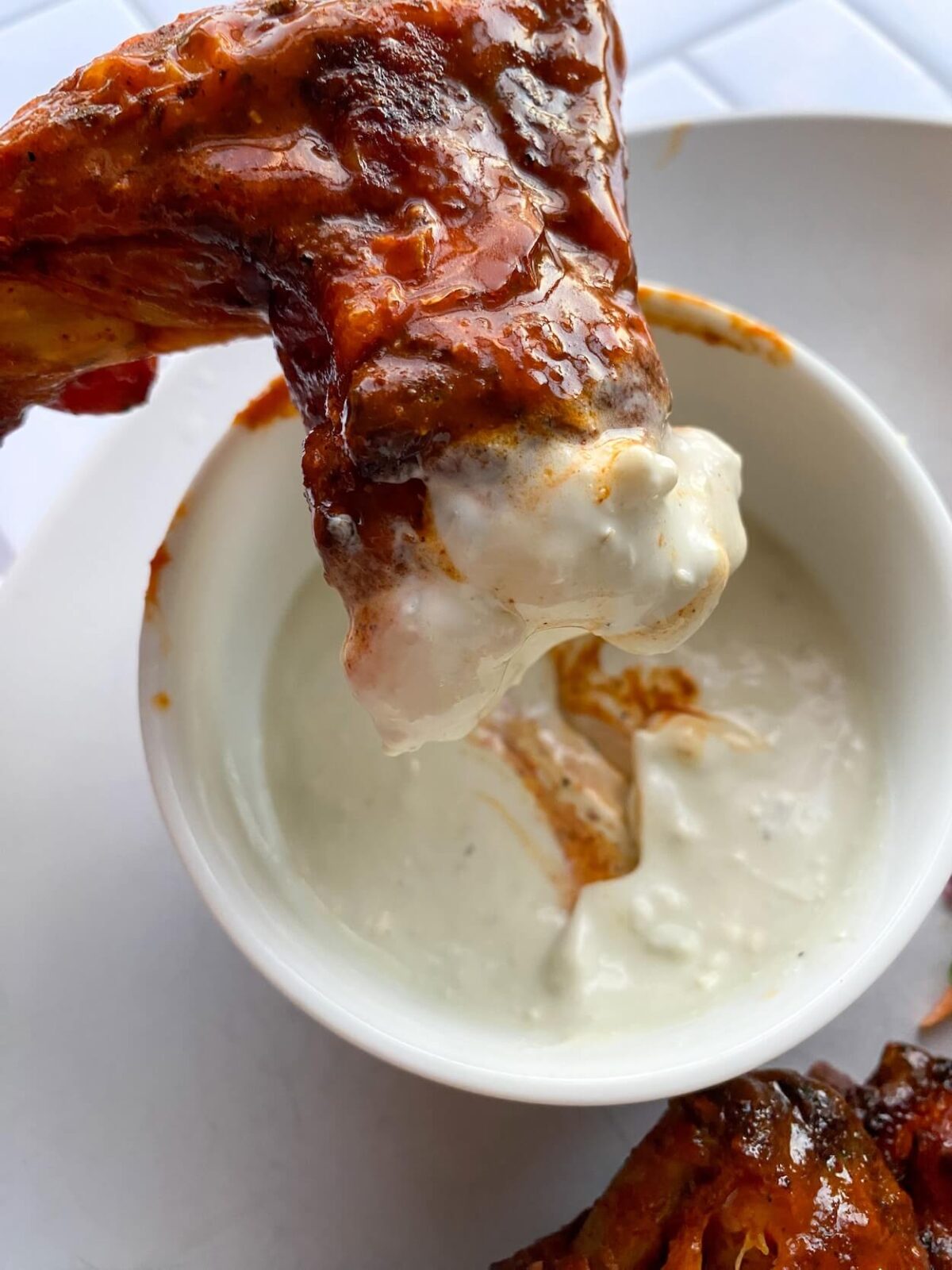 dipping a chicken wing into a small white bowl of creamy blue cheese wing dipping sauce.