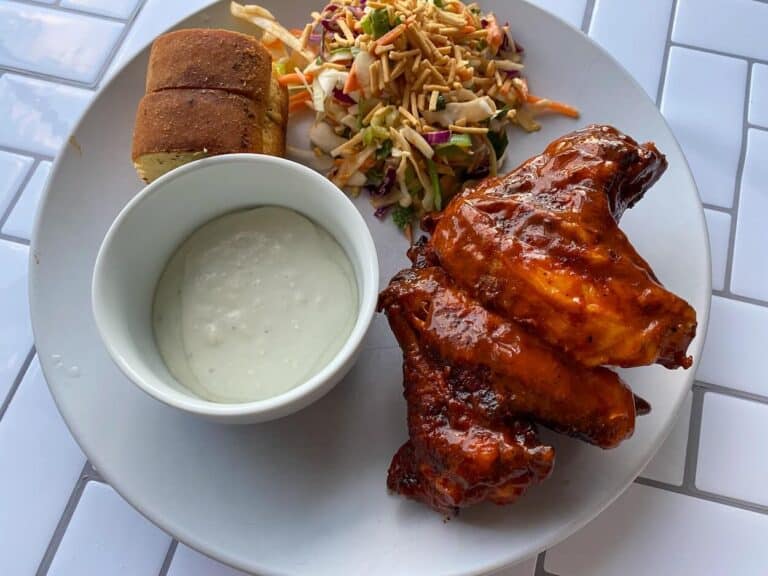 small bowl of blue cheese wing sauce on a plate with buffalo wings, salad and garlic bread.