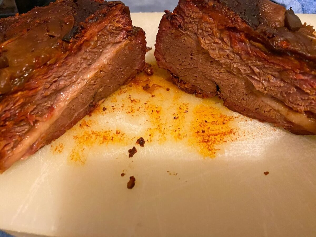 braised beef brisket cut in half on white cutting board. 