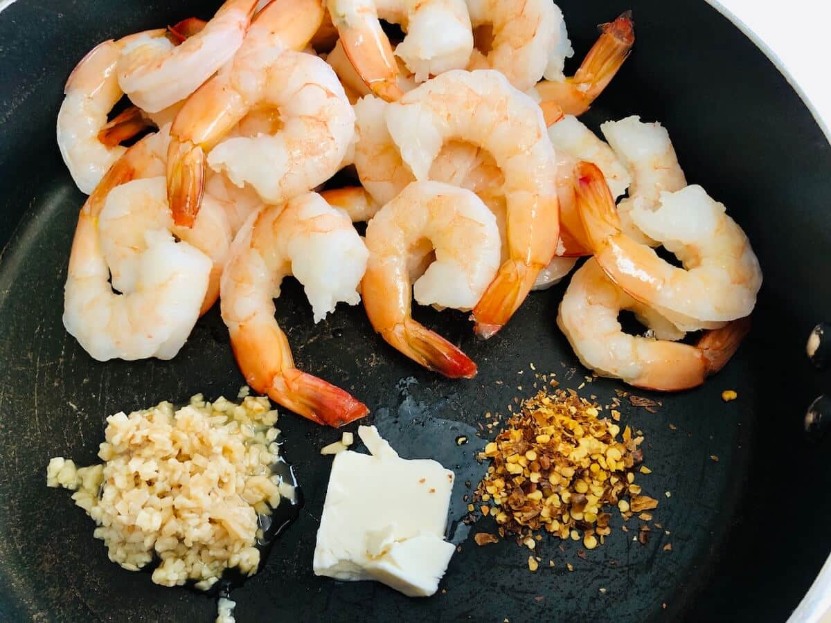 uncooked prawns in black skillet with butter, garlic and chilli ready to mix in.