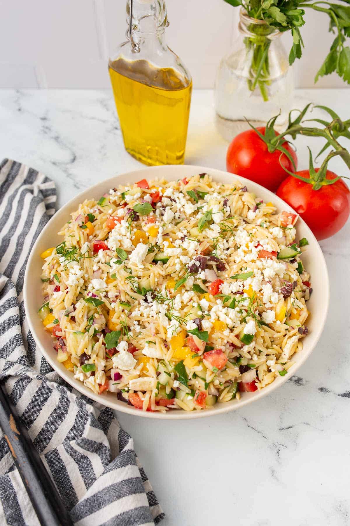 greek orzo salad in a white bowl with ingredients in background.