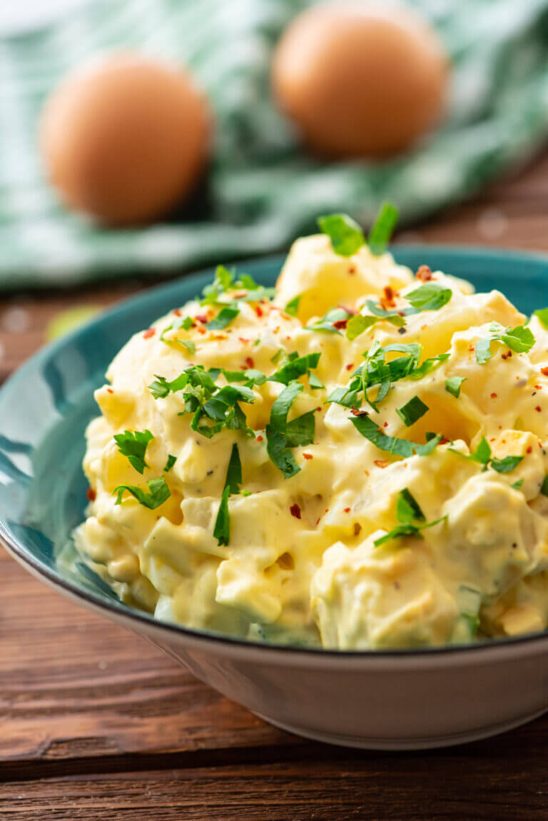 close up of potato salad in green bowl with eggs in background.