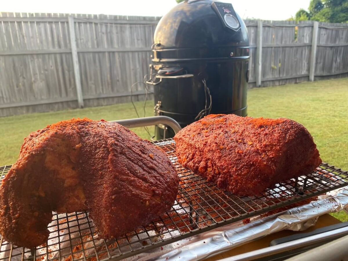 two seasoned beef briskets on a tray, with bullet smoker in background.