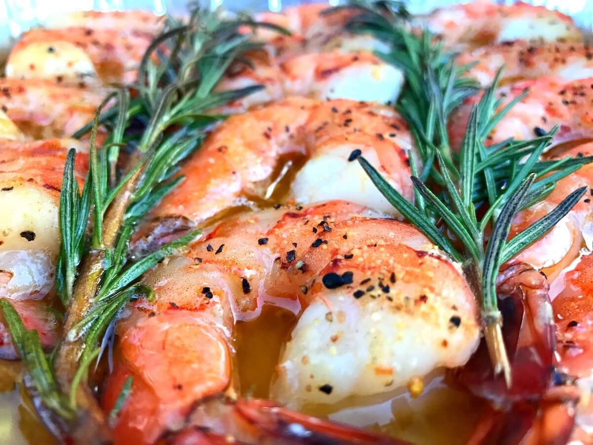 close up on buttery smoked shrimp with sprigs of rosemary.