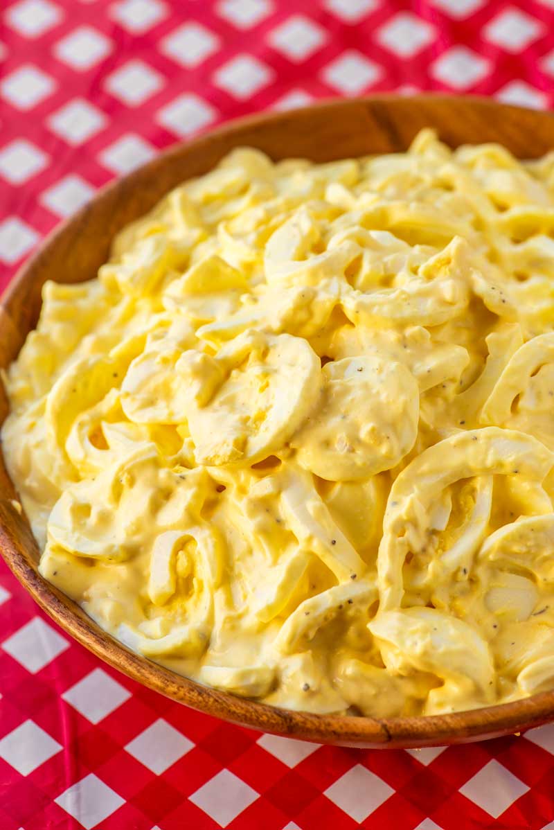 close up of egg salad in bowl on red checkered tablecloth.