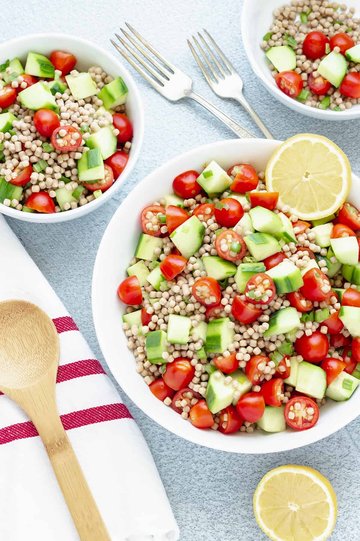 cucumber tomato salad in a large while bowl with two smaller serving bowls.