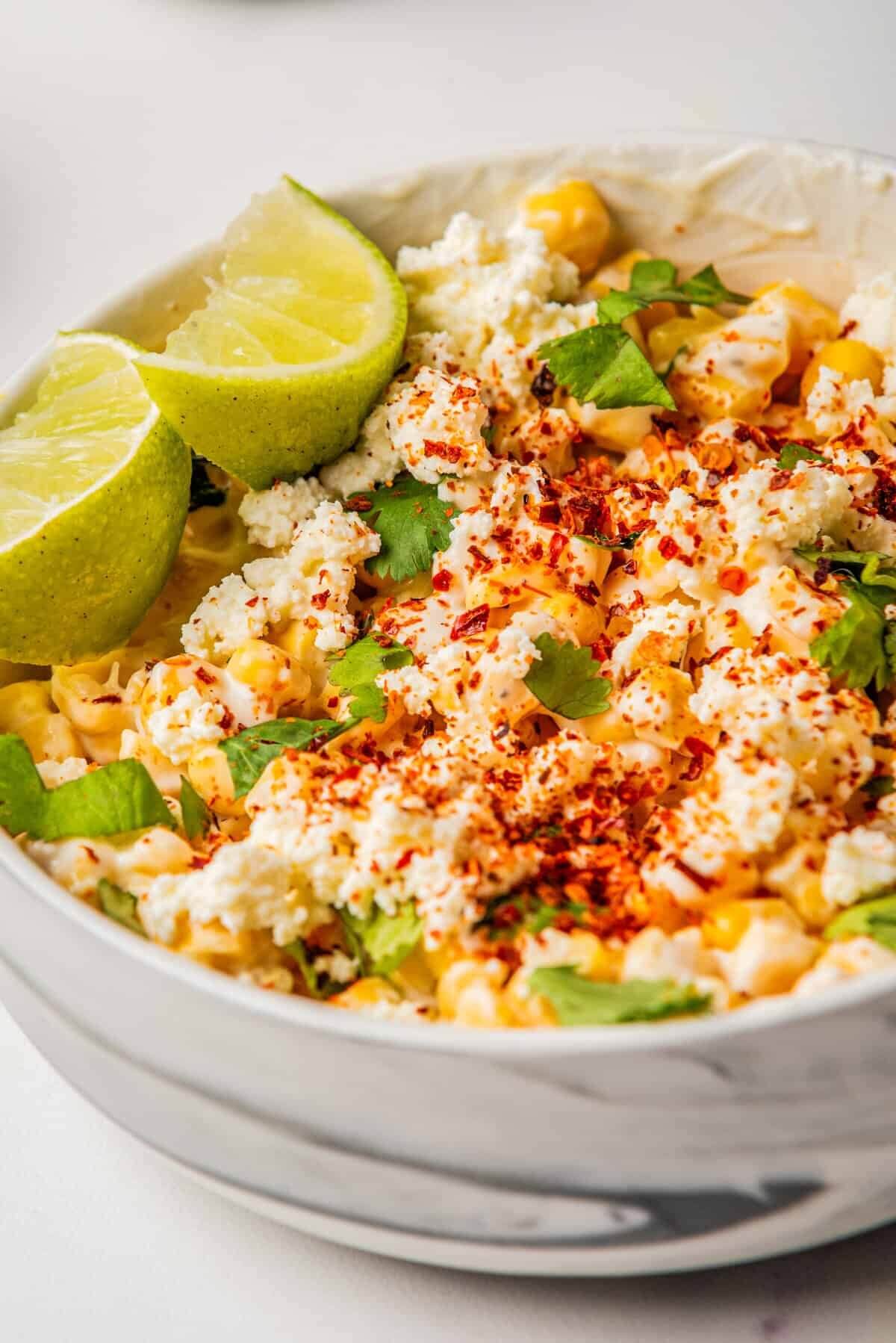 close up of mexican street corn salad with line slices in a white bowl.