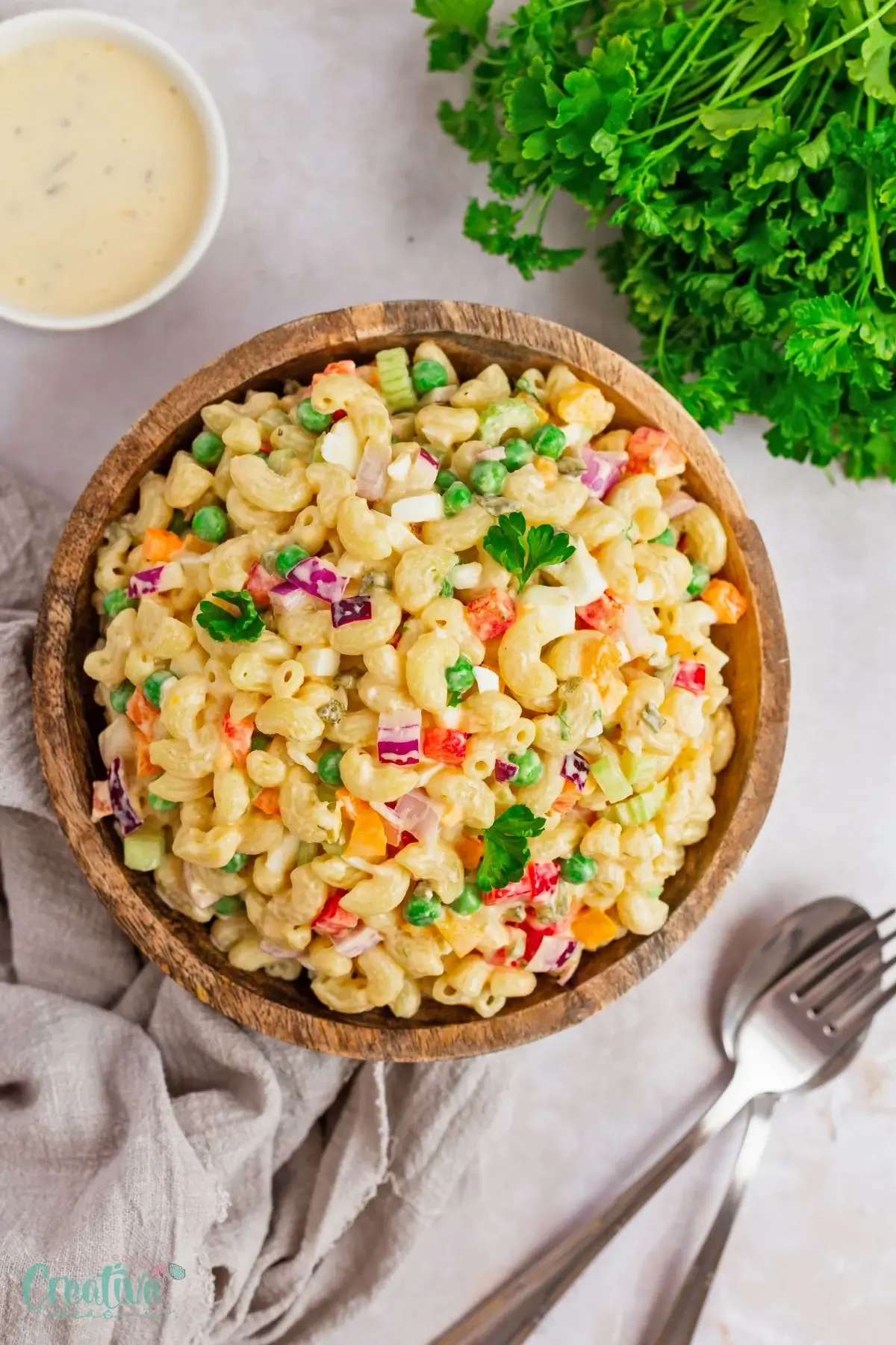 macaroni salad in a wooden bowl on a table with cutlery and fresh herbs.