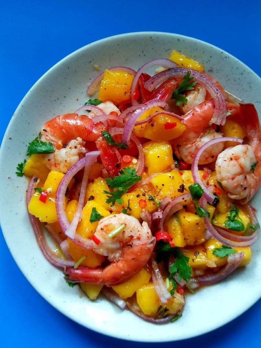 spicy prawn mango salad in white bowl on blue background.