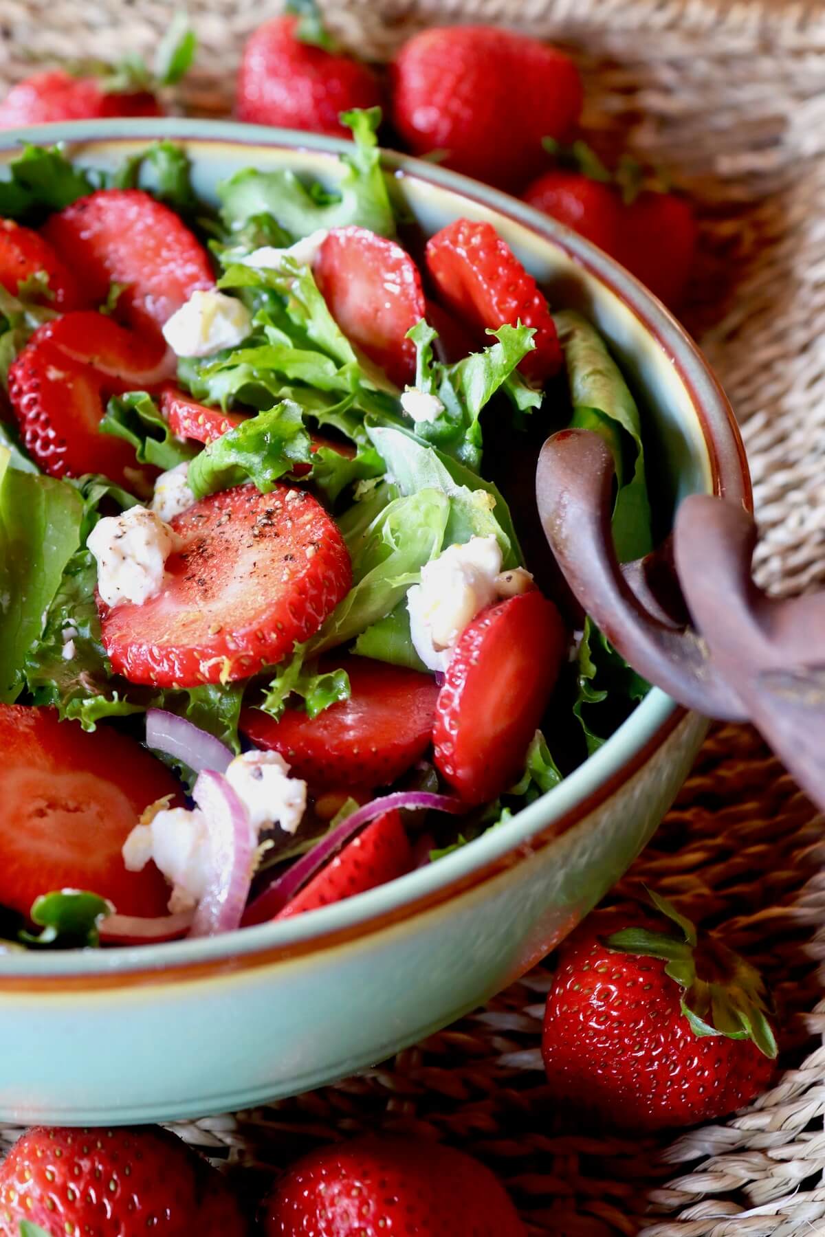 close up of strawberry goat cheese salad in a white bowl surrounded by strawberries.