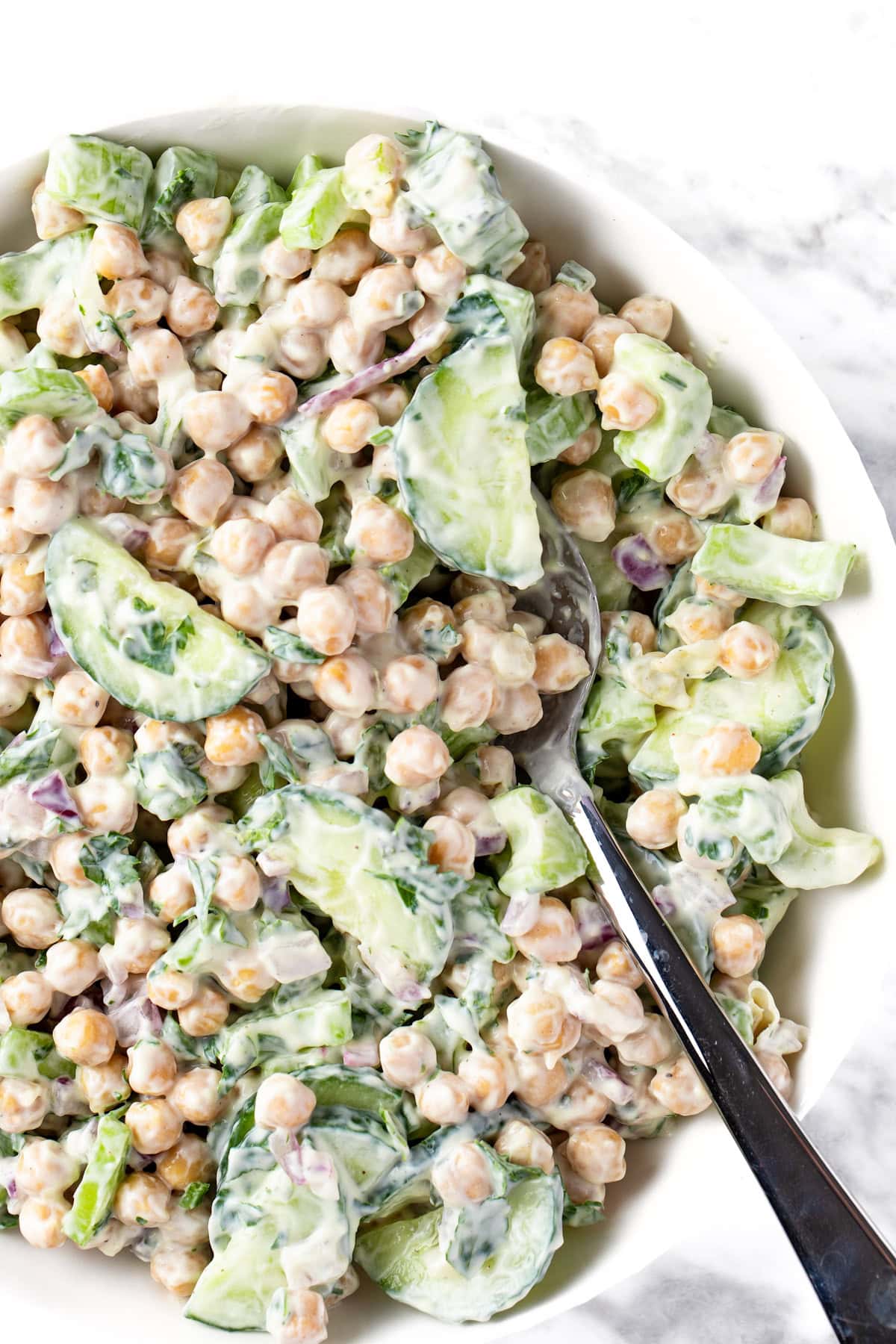 creamy chickpea salad in a white bowl with spoon.