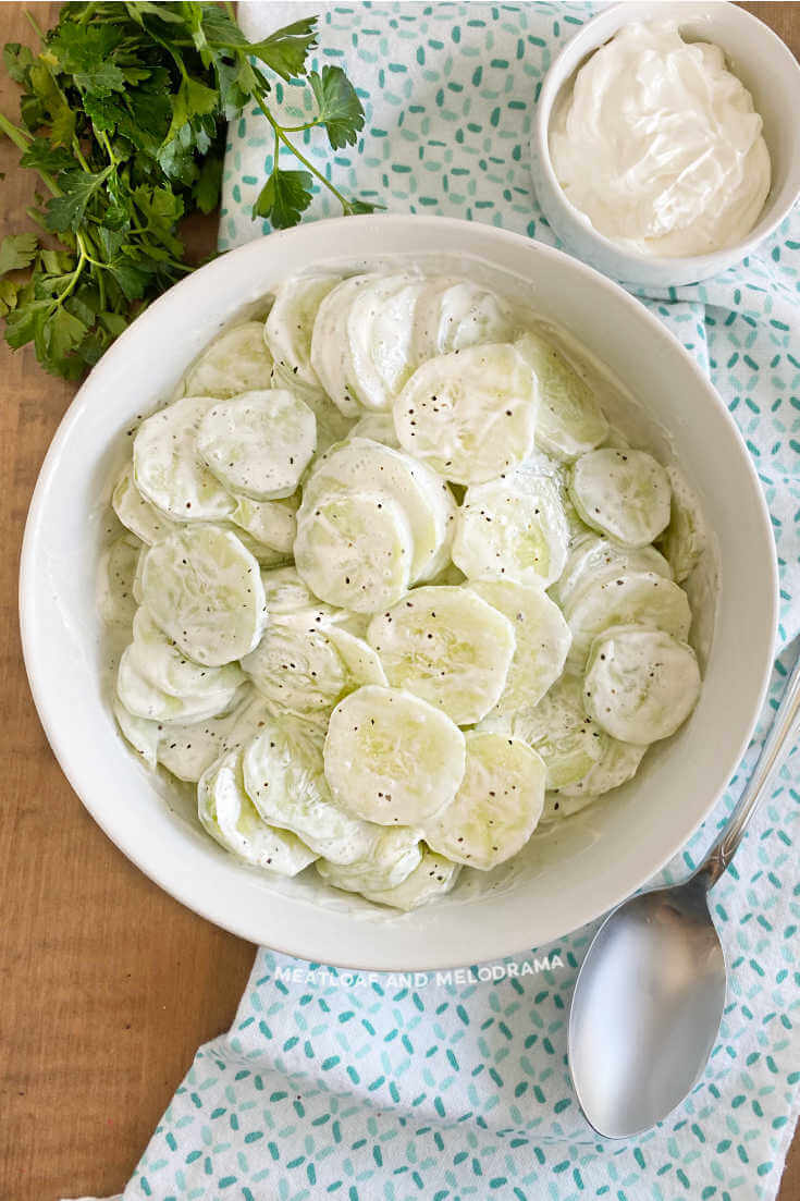 creamy cucumber salad in a white bowl with tea towel and spoon.