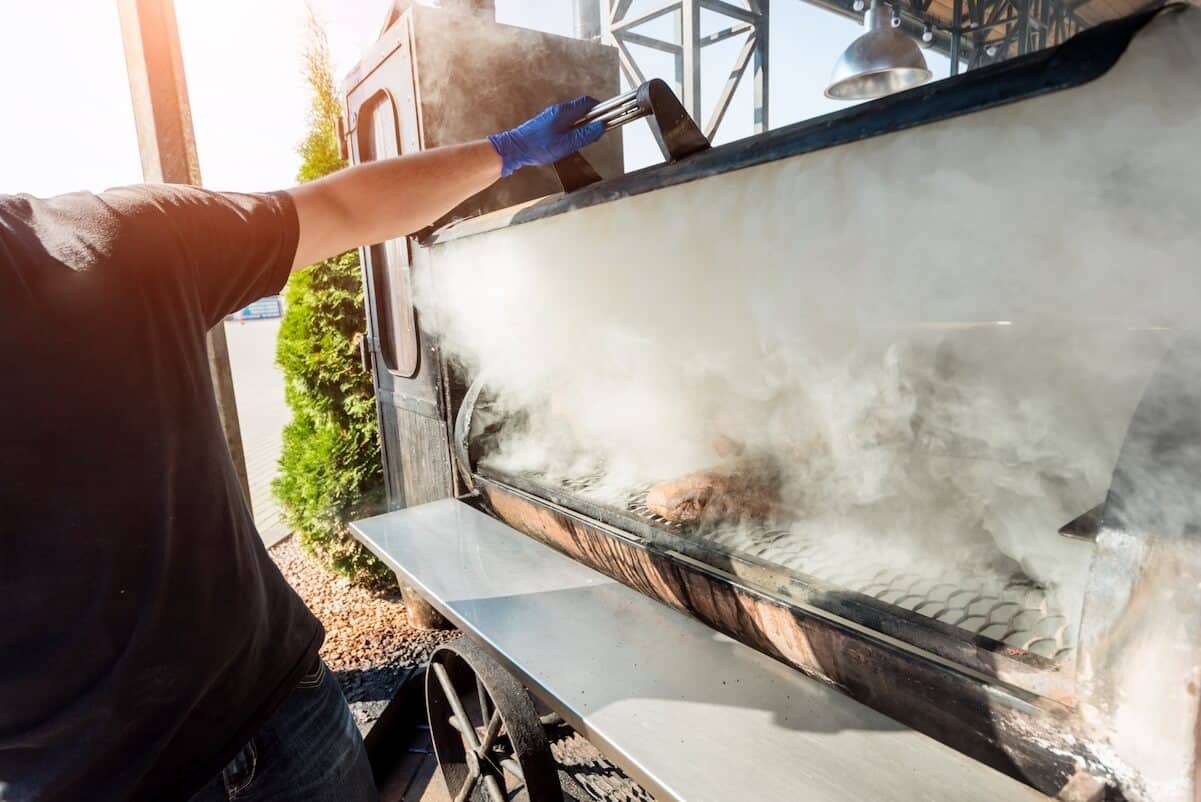 man lifting lid on large smoker with smoke billowing out.