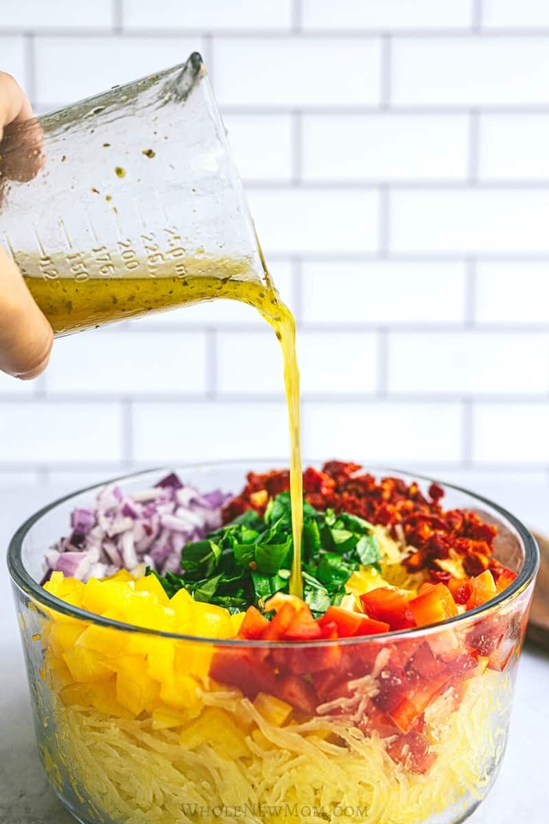 spagetti squash salad ingredients in a glass bowl as dressing is poured over.