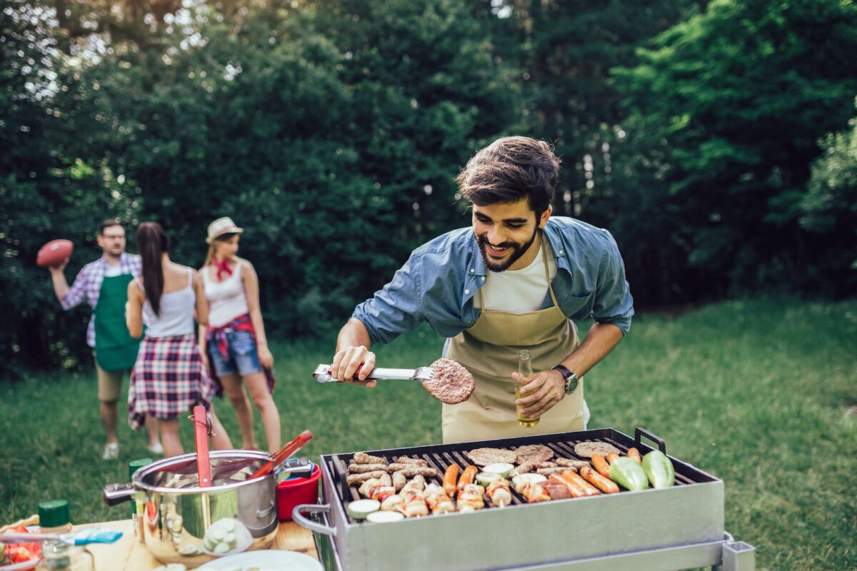 BBQ party with man at grill and friends in background playing football.