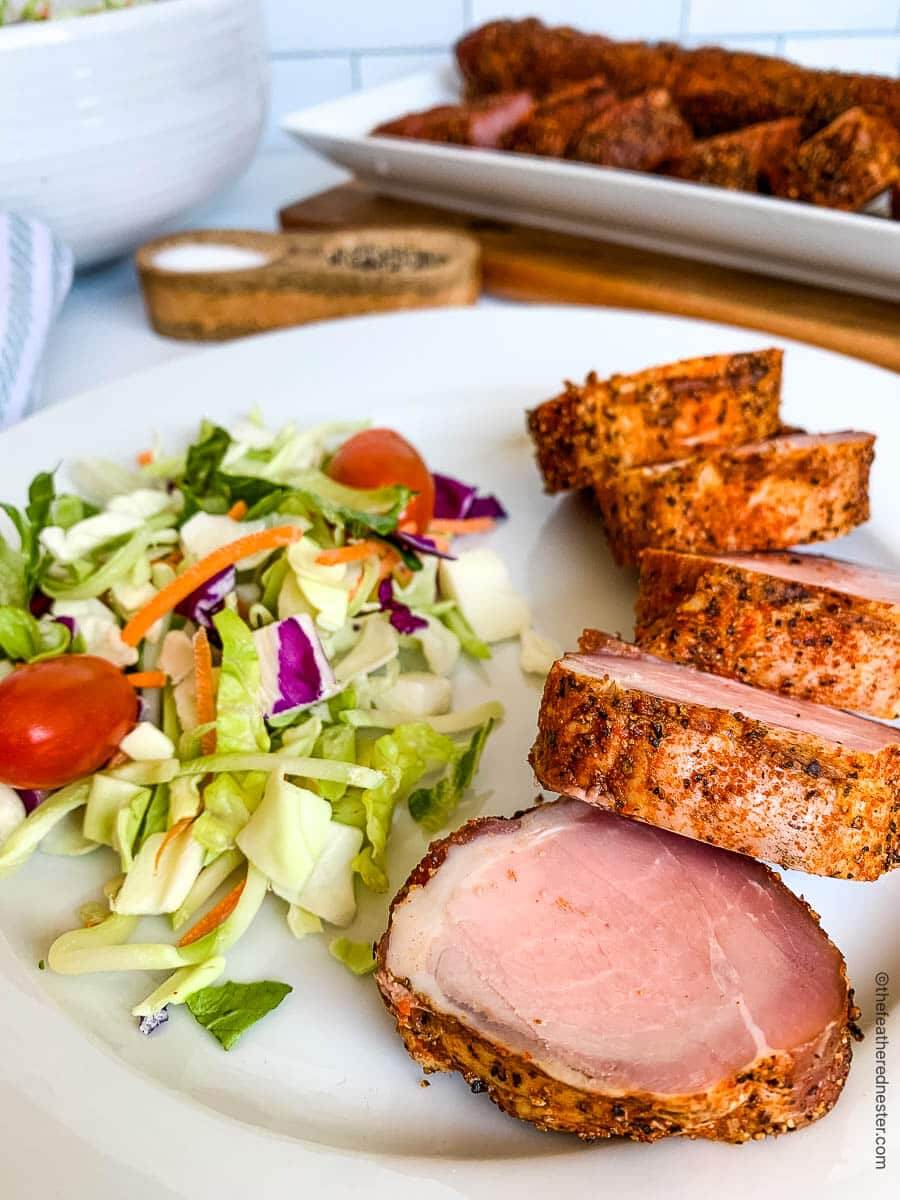 smoked pork tenderloin close up on place, sliced, with side salad.